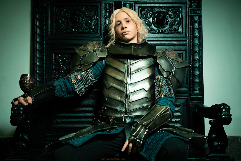 Aegon Targaryen in armor, slouched on a dark carved throne with a goblet