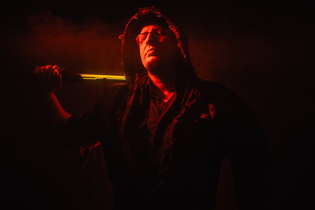 Kuba 'Pirozek' Ludwig in a hooded coat holding a katana over his shoulder, lit by a single red light