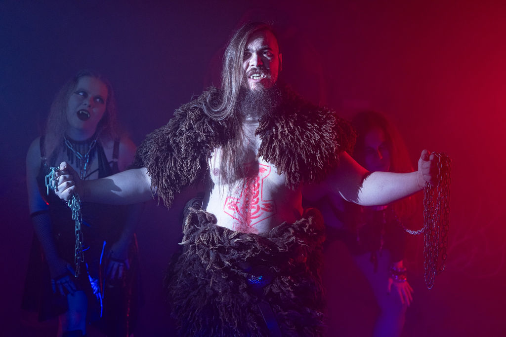 Three vampires reaching through fog with chains, lit in red and blue